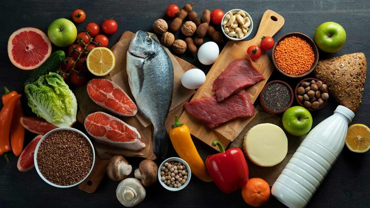 A colorful assortment of traditional Blue Zone diet foods including organic beans, barley grains, wild greens, and regional olive oil.