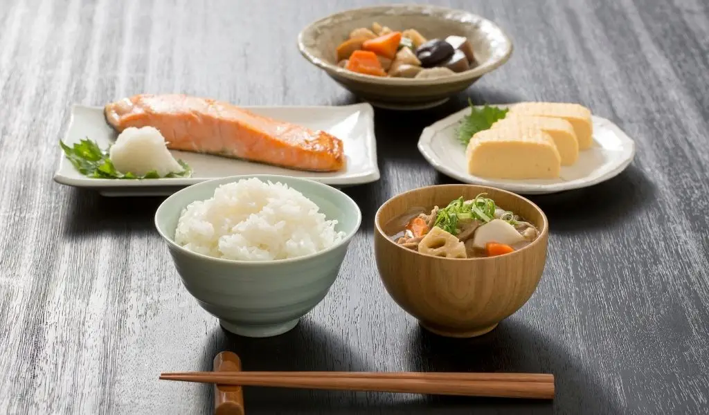 A traditional Japanese Washoku meal featuring dashi broth, steamed rice, grilled fish, seaweed salad, and green tea.