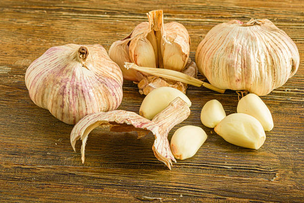 Fresh organic garlic bulbs and crushed garlic cloves on a wooden board, releasing bioactive allicin organosulfur compounds.