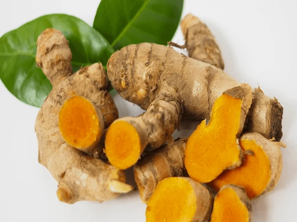 Fresh raw turmeric root sliced open alongside whole black peppercorns and extra virgin olive oil for maximum curcumin bioavailability.