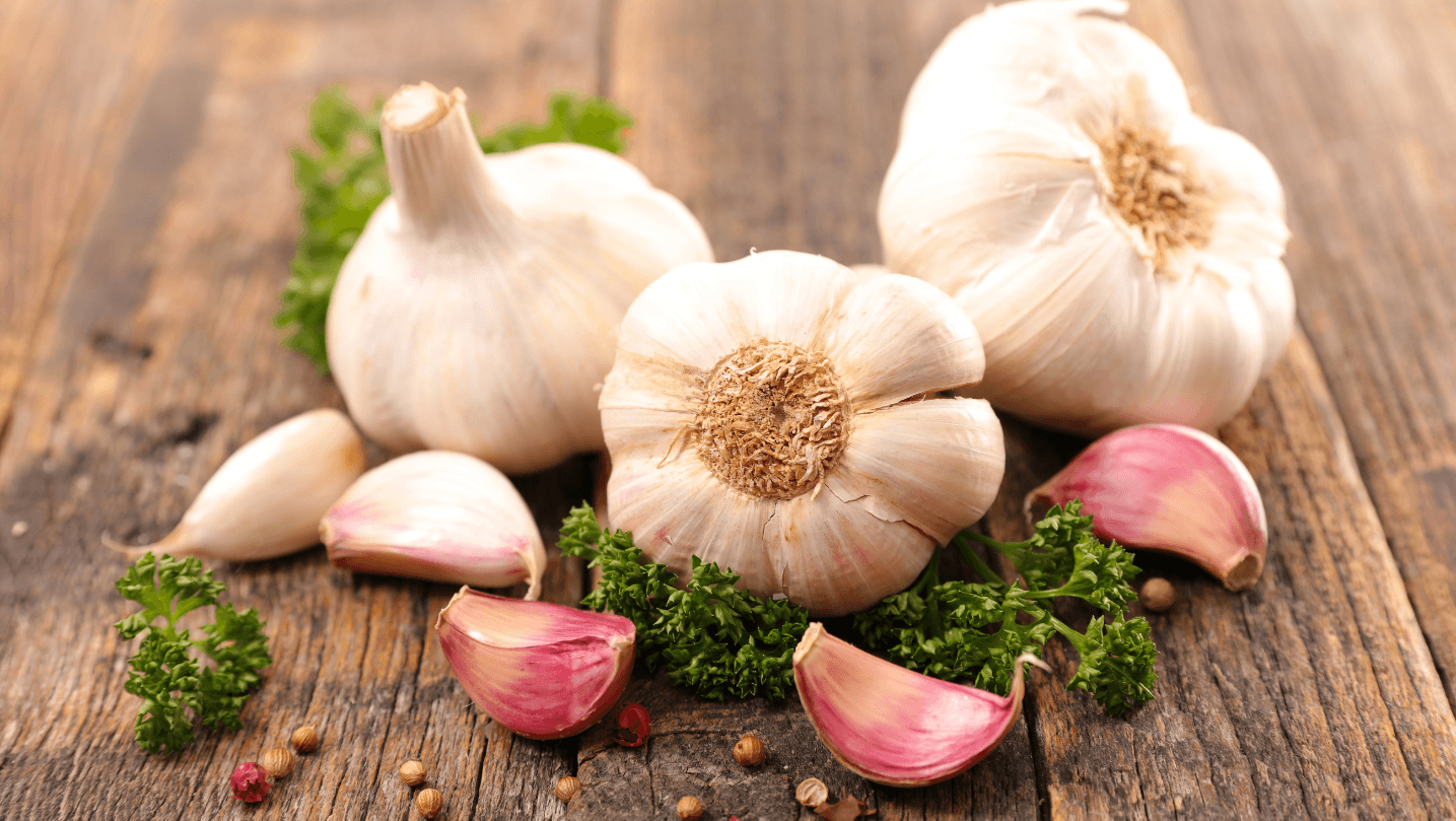 Whole white garlic bulbs and peeled cloves on a dark stone counter, rich in immune-boosting allicin and organosulfurs.
