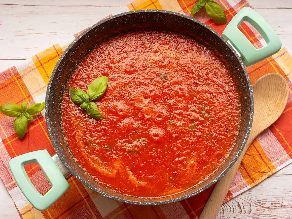 A simmering pan of rich red Classic Pomodoro Sauce garnished with fresh green basil leaves and extra virgin olive oil.