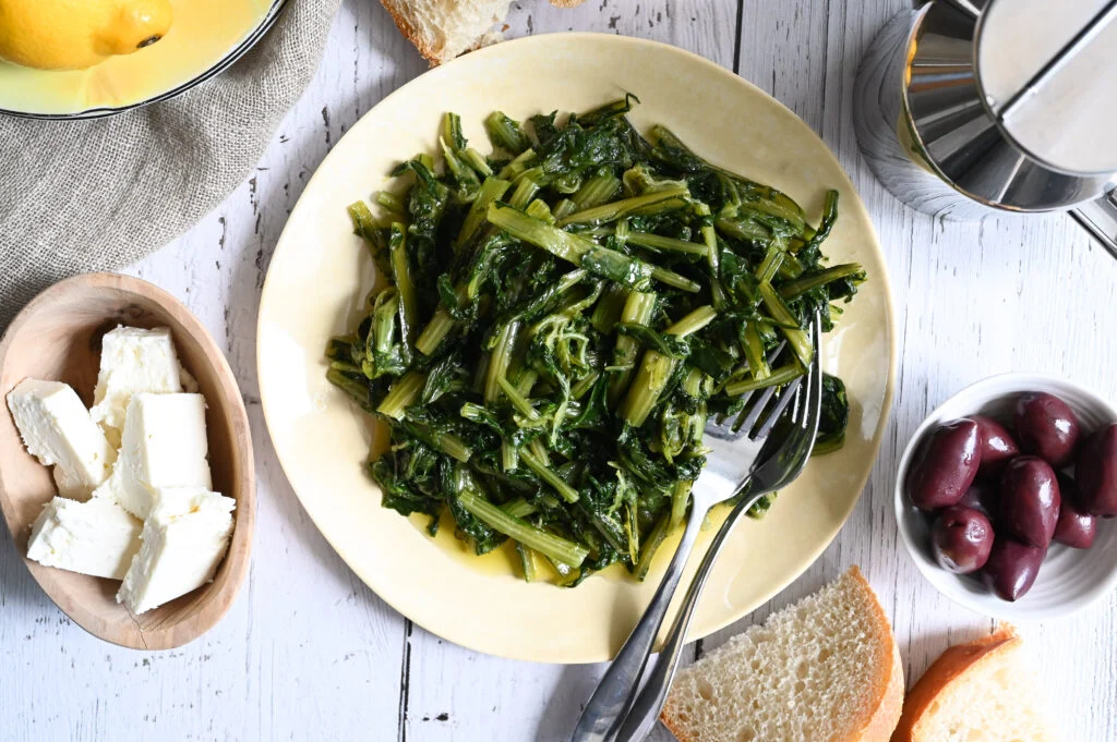 Steamed Greek Horta wild greens dressed with fresh lemon juice and cold-pressed olive oil, rich in fat-soluble vitamins A, K1, and E.